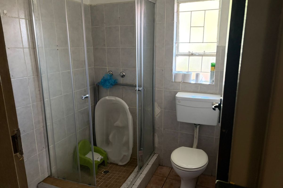 A compact bathroom featuring a glass-enclosed shower, a standard toilet, and tiled walls and flooring.