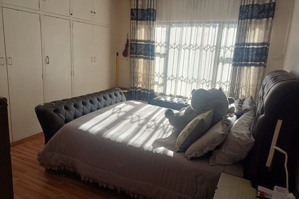 A bedroom featuring built-in cupboards, laminate flooring, and a large window with security gate, providing natural light.