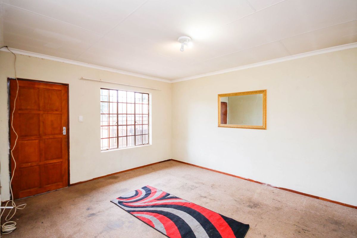A vacant bedroom featuring carpet flooring, a wooden door, and a window with security bars.