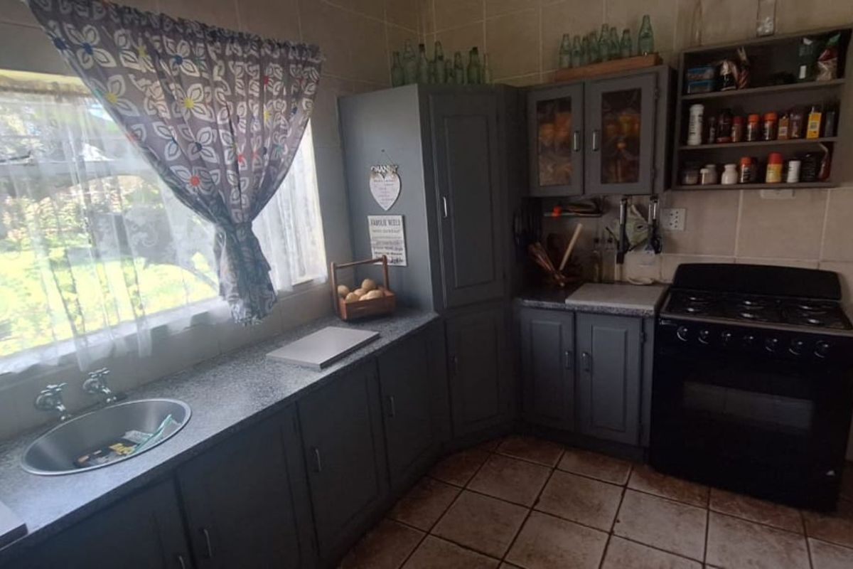A functional kitchen featuring grey cabinetry, a built-in stove, tiled flooring, and a stainless steel sink overlooking the garden.
