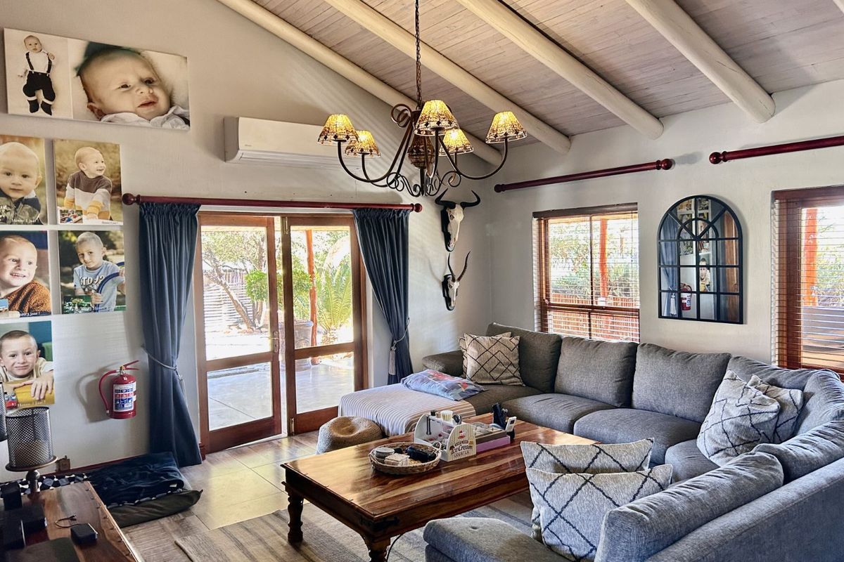 A cozy living room featuring exposed timber ceiling beams, a split-system air conditioner, and double glass doors leading to an outdoor patio area.