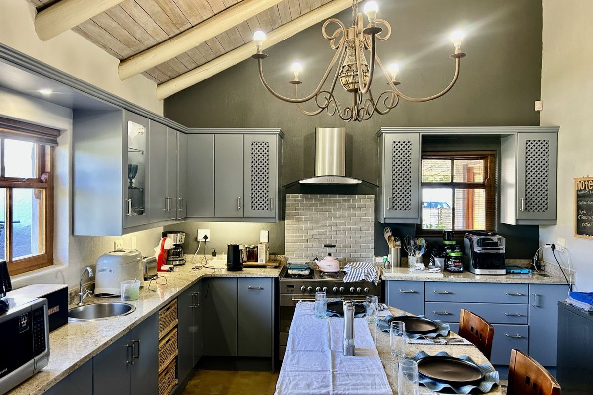 A well-appointed kitchen featuring grey cabinetry, granite countertops, a subway tile backsplash, stainless steel extractor fan, and a vaulted timber-beamed ceiling.