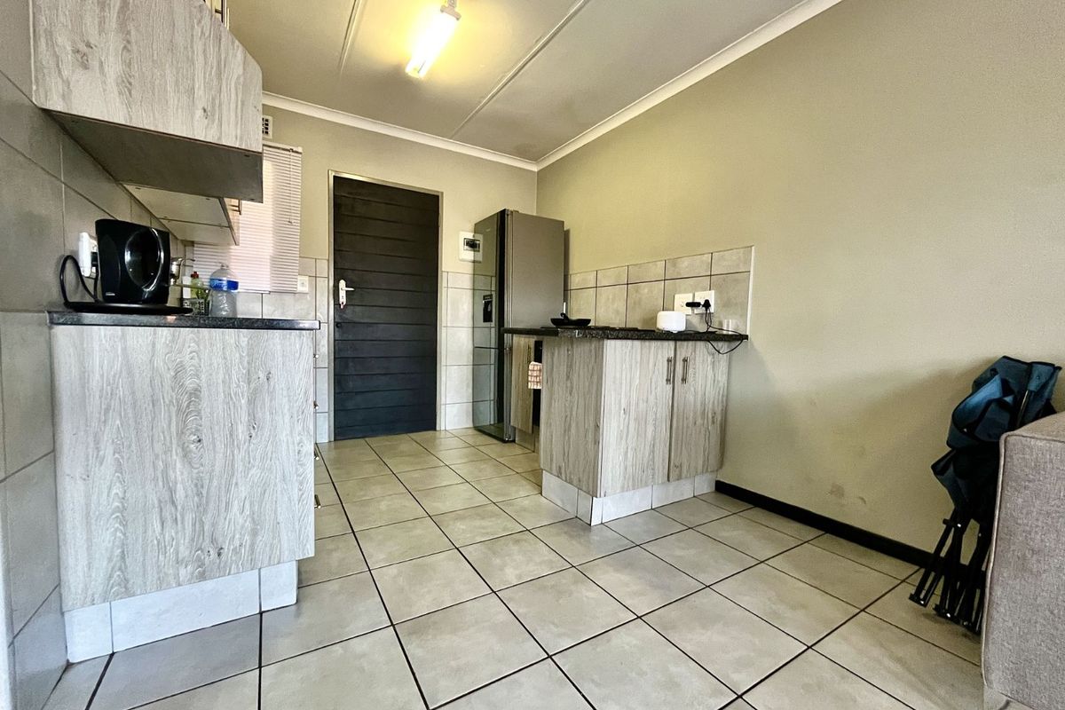 A functional kitchen area featuring wood-look cabinetry, dark countertops, tiled flooring, and a direct access door.