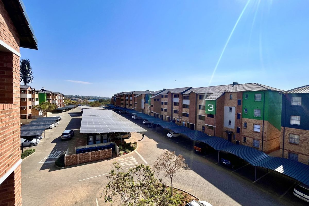 Elevated view of an apartment complex featuring multi-story brick buildings, paved parking areas, and solar panel carports.