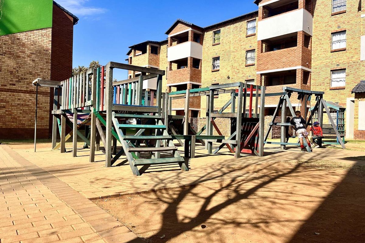 Communal outdoor play area featuring a timber jungle gym and swing set situated within the apartment complex grounds.