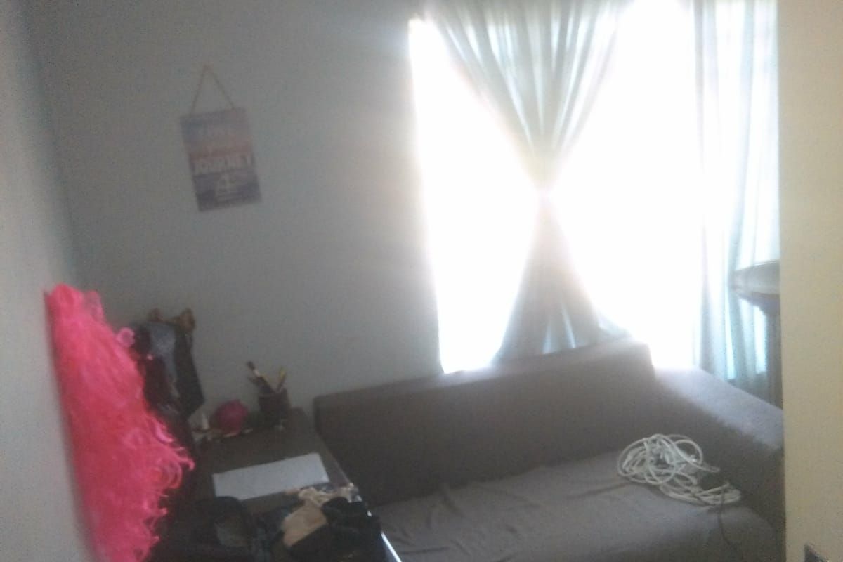 A bedroom featuring a window with curtains, providing natural light. The room includes basic finishes and requires some maintenance.