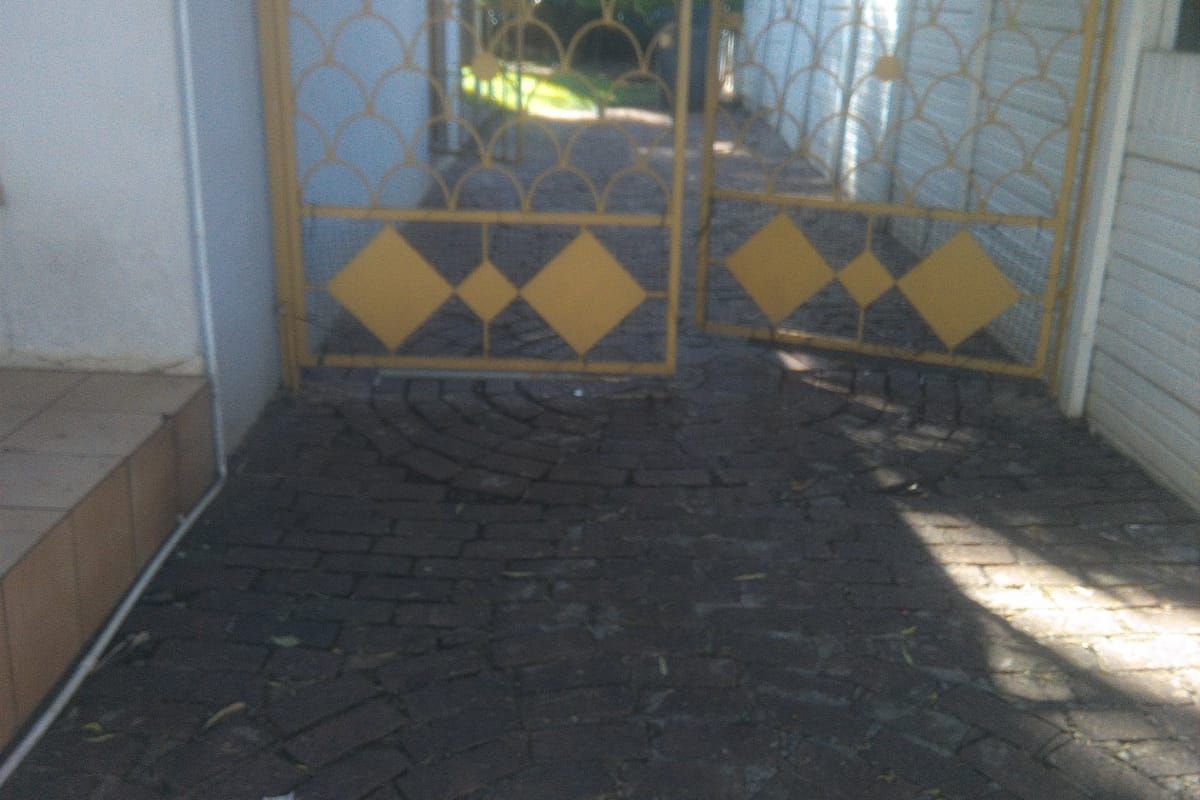 Side access area featuring decorative metal security gates, paved driveway, and perimeter walling with security wire.