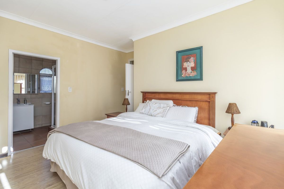 A well-maintained bedroom featuring light-toned laminate flooring, neutral walls, and an en-suite bathroom with tiled finishes.