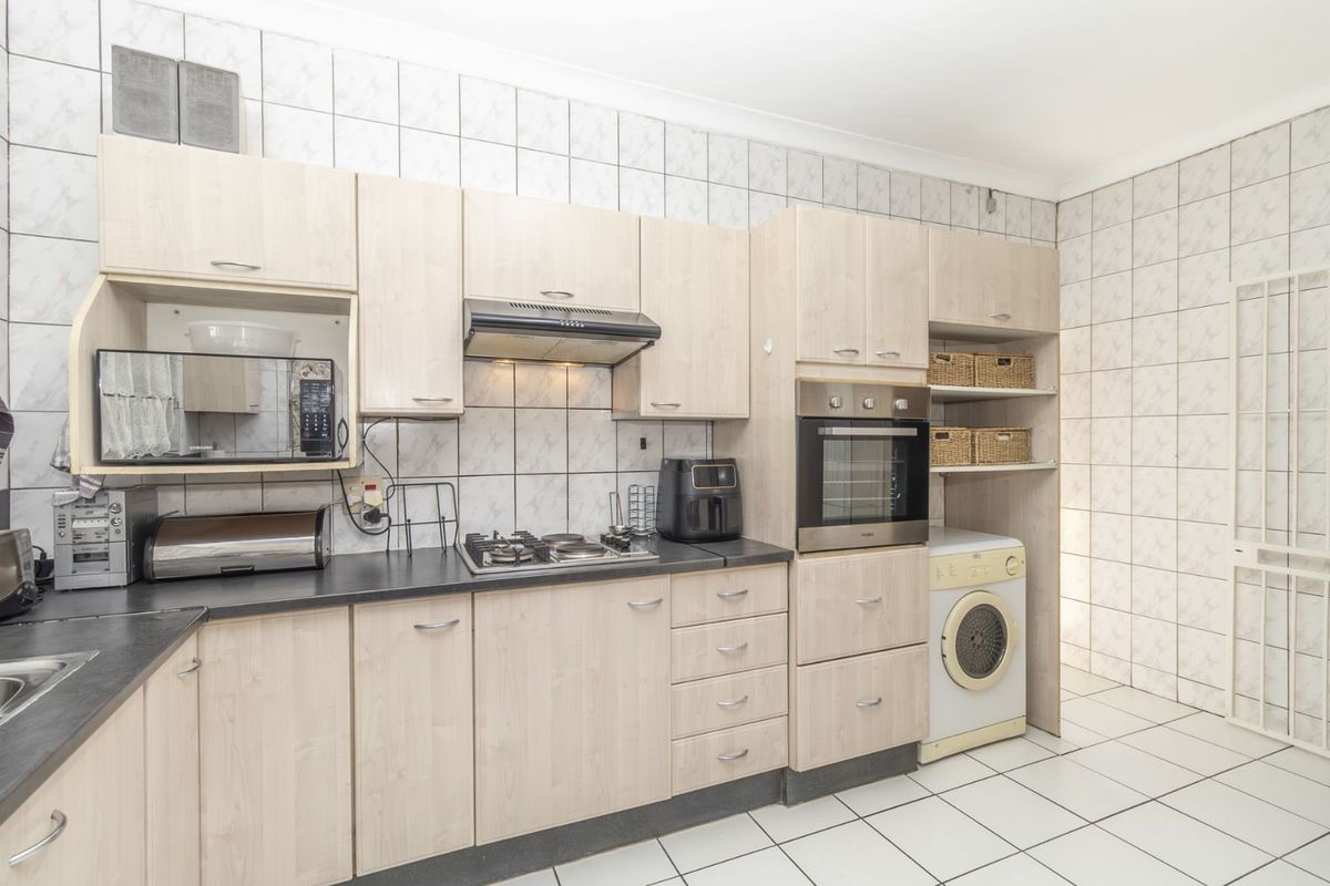 Functional kitchen featuring light wood-look cabinetry, built-in oven, gas hob, extractor fan, and integrated laundry space with tiled flooring and walls.