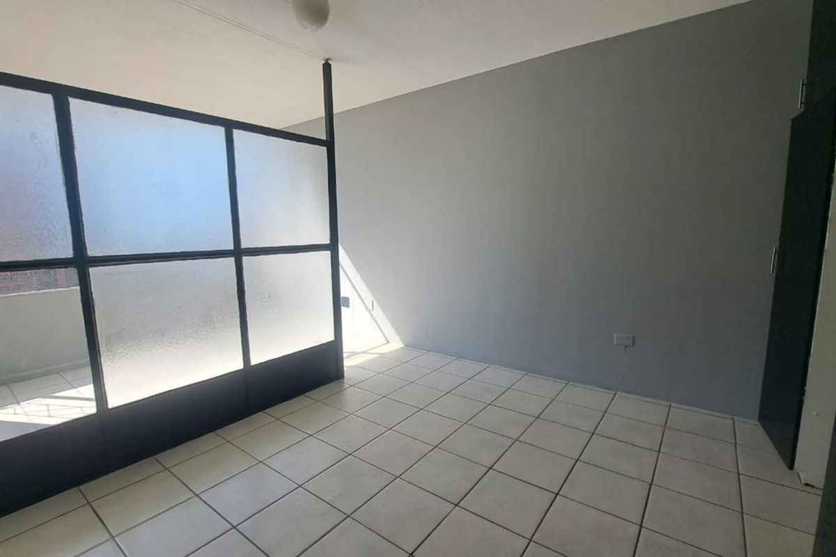 An empty living area featuring tiled flooring, a modern frosted glass room divider, and a built-in cupboard, offering a versatile and neutral space.