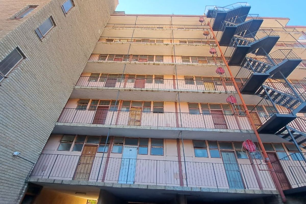 Exterior view of an apartment building featuring multi-level balcony walkways and an external metal fire escape staircase.