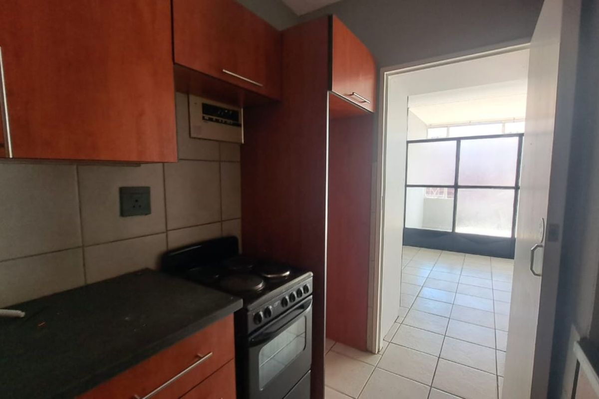 A compact kitchen featuring laminate cabinetry, a tiled backsplash, and a built-in electric stove, leading into an adjacent tiled living area.
