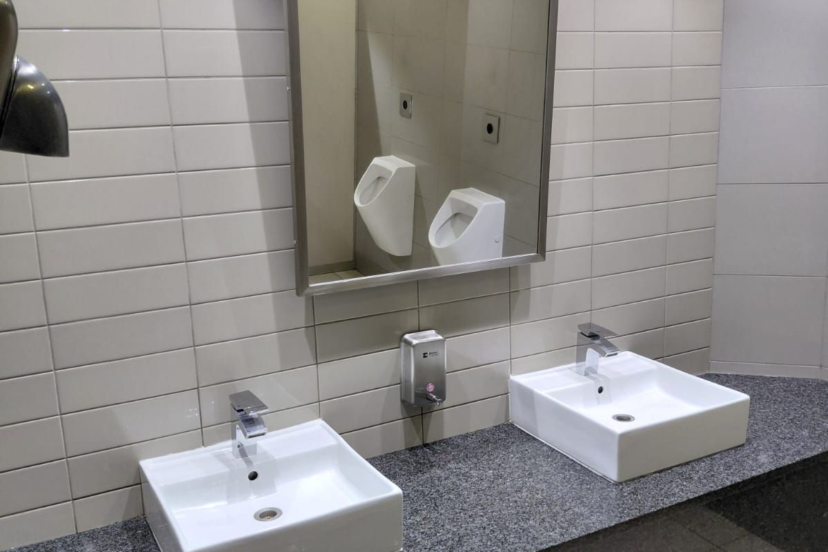 A clean office restroom featuring a granite vanity countertop with dual vessel sinks, chrome faucets, and a large wall-mounted mirror.