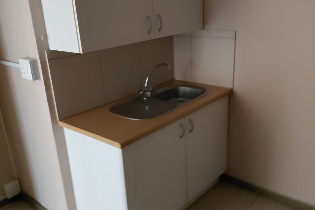 A compact kitchenette area featuring built-in white cabinetry, a laminate countertop, and a stainless steel sink with a mixer tap.
