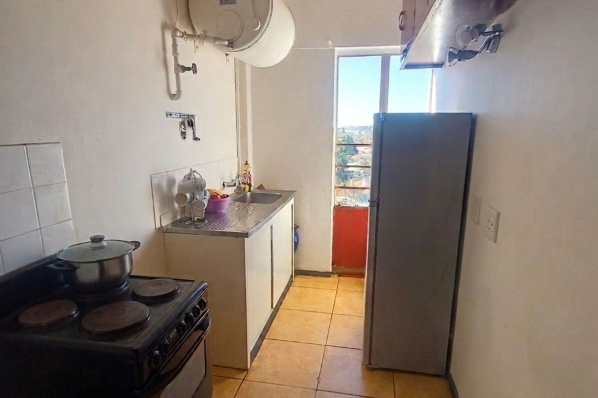 A compact kitchen featuring basic cabinetry, a stainless steel sink, and an electric stove, with an adjacent door leading to a balcony area.