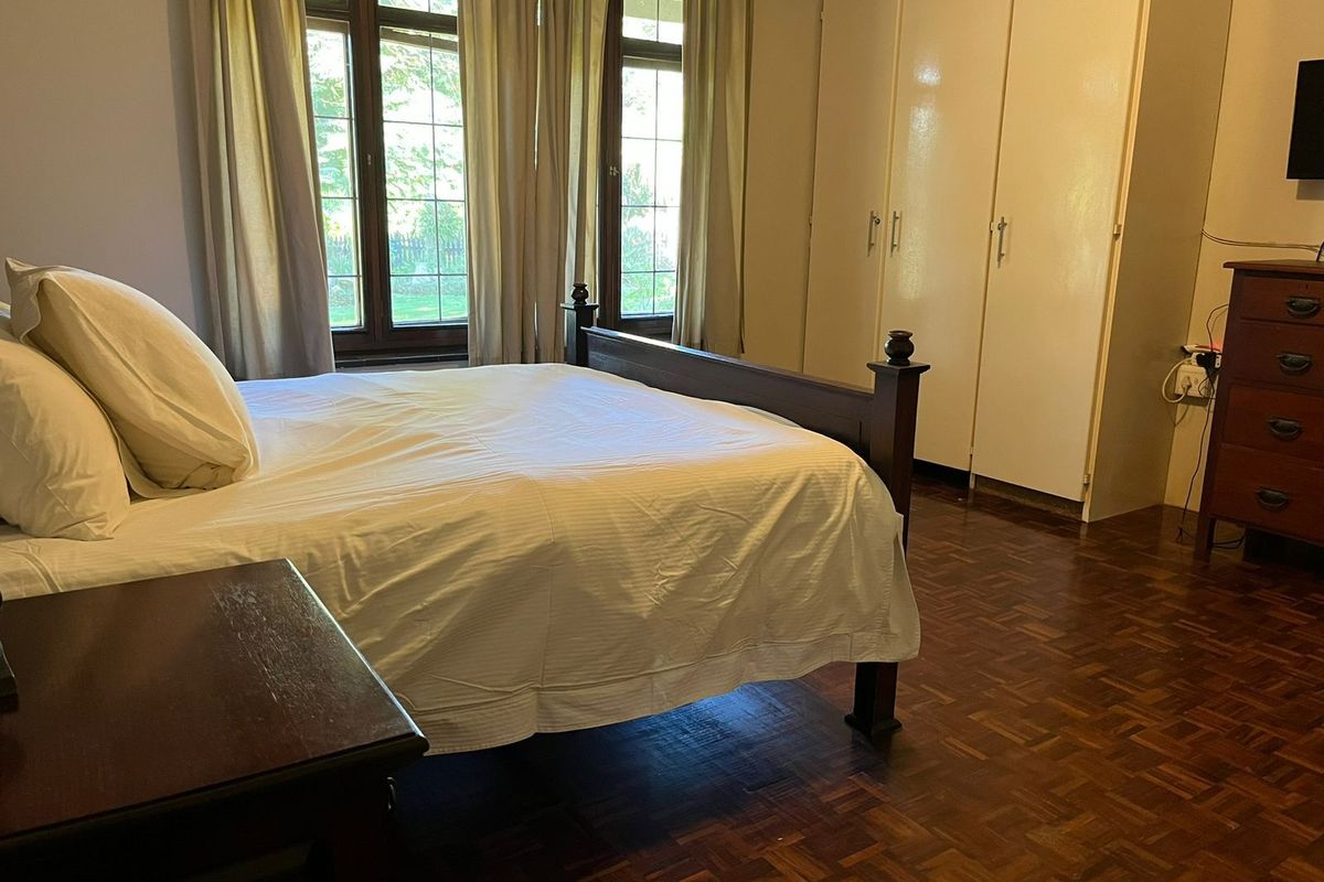 A bedroom featuring polished parquet flooring, built-in cupboards, and large windows allowing natural light.