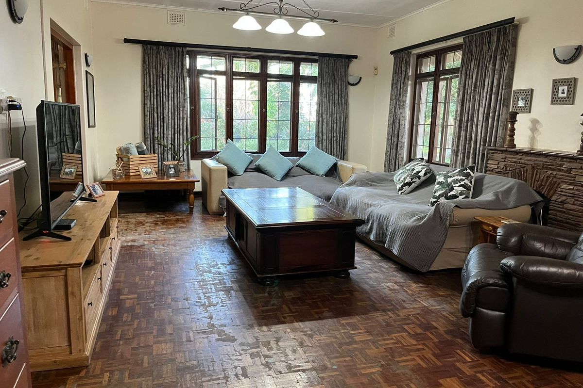 Spacious living room featuring traditional parquet flooring, large timber-framed windows, and a built-in stone fireplace surround.