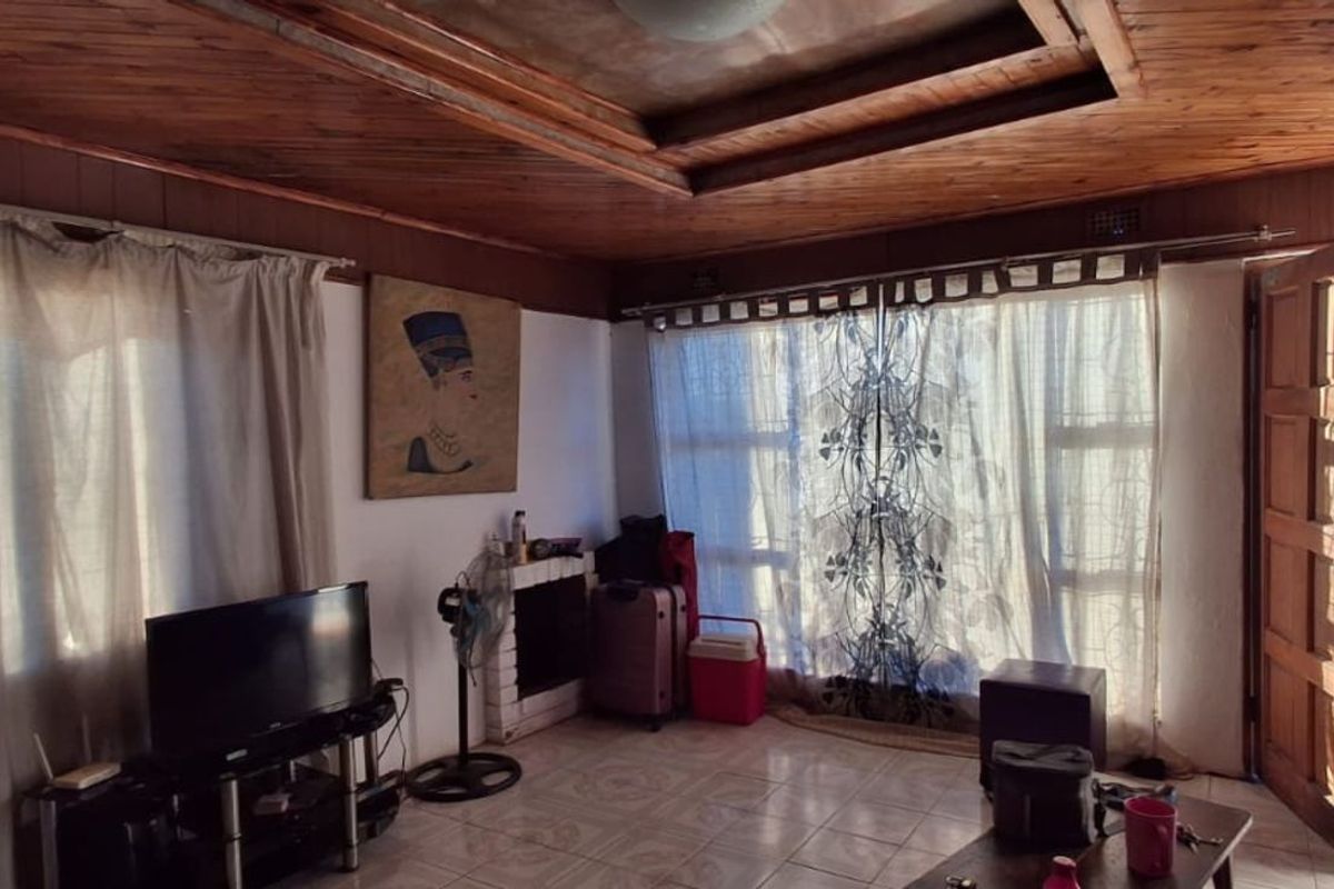 A living room featuring a distinctive wood-paneled ceiling, tiled flooring, and direct access to the exterior through a wooden door.