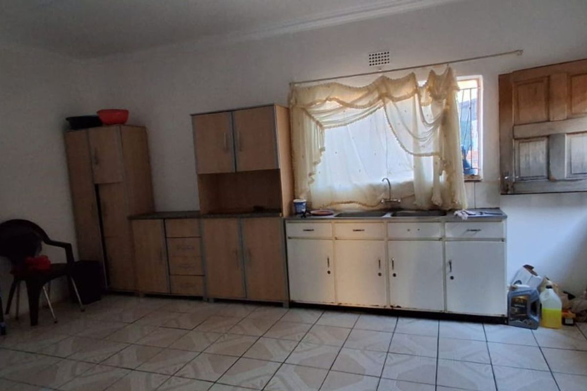 A dated kitchen featuring basic cabinetry, a double sink, and tiled flooring, offering a functional space with significant potential for modernization and renovation.