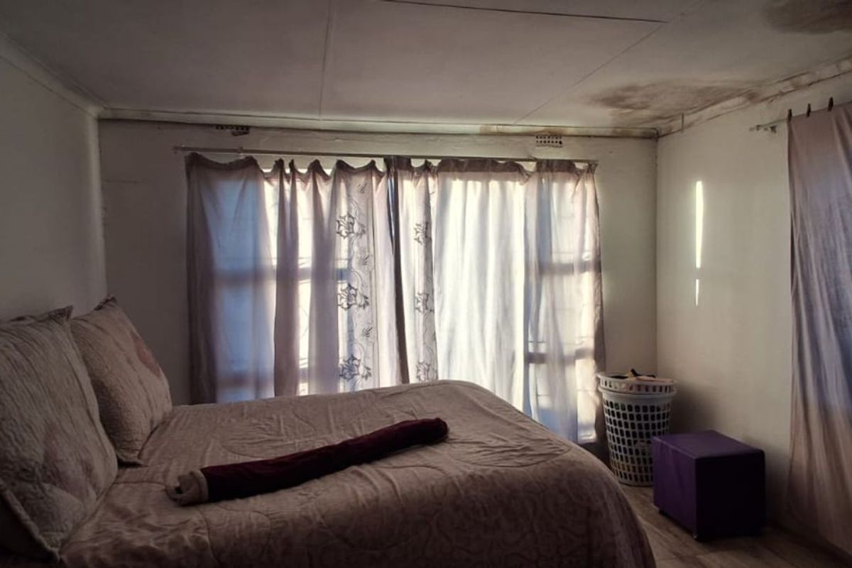 A bedroom featuring large windows with curtains and visible signs of ceiling water damage requiring maintenance and repair.
