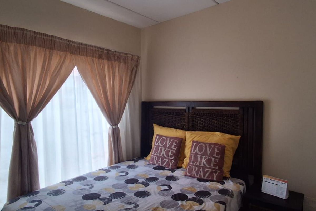 A standard bedroom featuring neutral wall tones, a large window with curtains, and built-in cupboard space.
