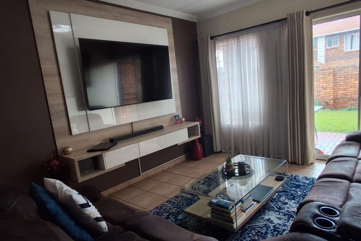 A comfortable living room featuring a modern built-in media wall unit, tiled flooring, and large sliding glass doors providing access to the rear garden.