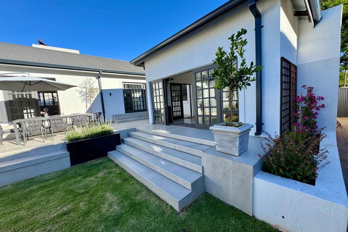 A well-maintained rear exterior featuring a paved patio, concrete steps, landscaped garden beds, and French doors leading into the home.