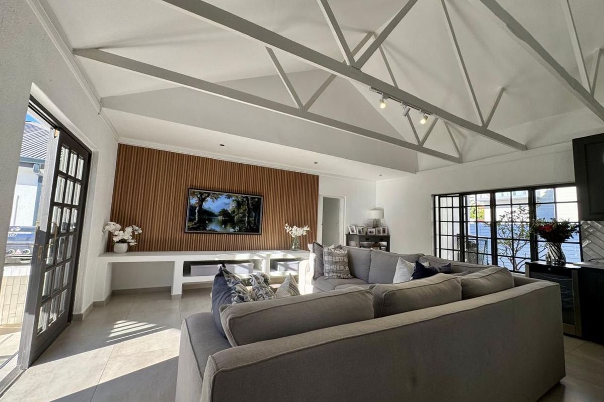 Spacious living room featuring a high vaulted ceiling with exposed trusses, a modern timber-slat feature wall, and large glass doors leading to the exterior.