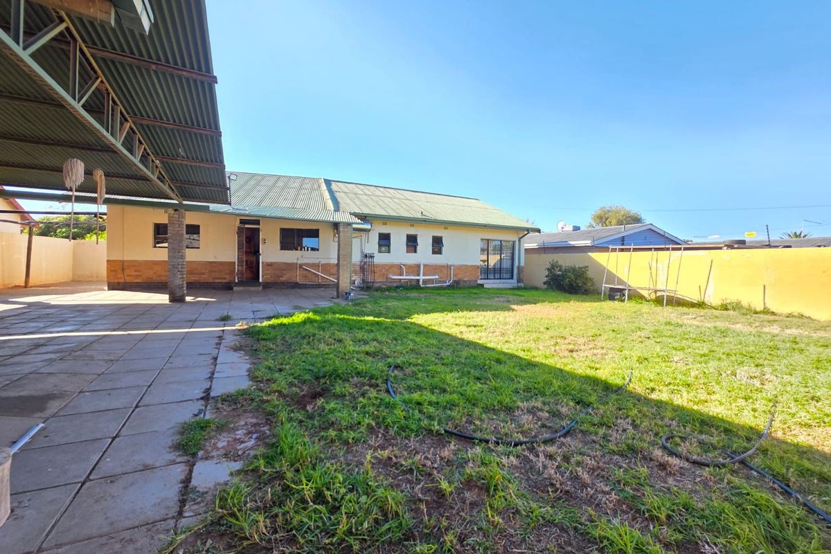 Spacious rear garden featuring a large covered patio area, paved flooring, and a generous lawn space, ideal for outdoor living and entertaining.
