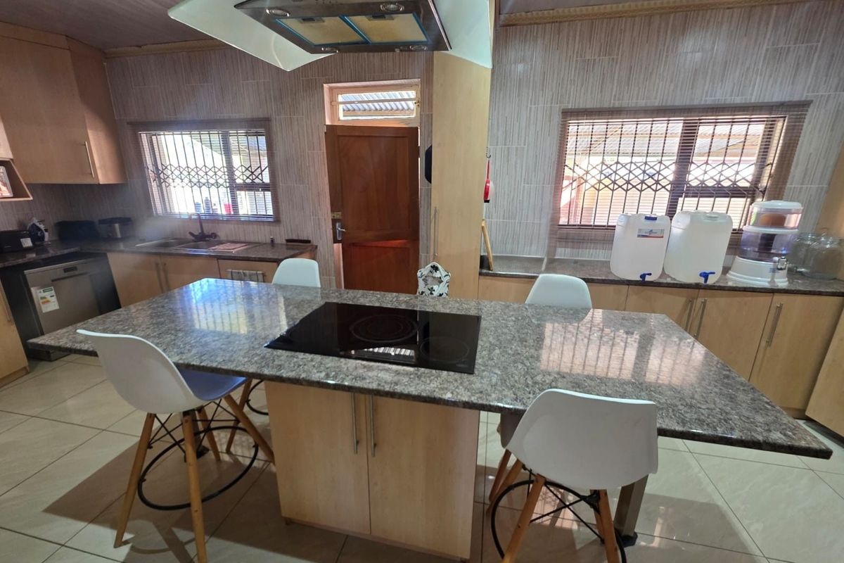 A functional kitchen featuring a central island with a built-in electric hob, granite countertops, light wood cabinetry, and a modern extractor fan.