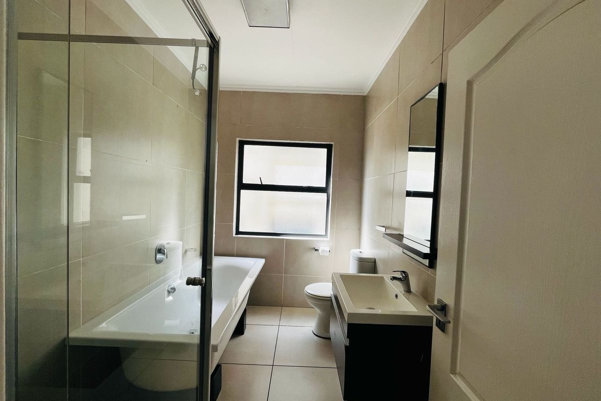 A functional bathroom featuring a glass-enclosed shower, a bathtub, a wall-mounted vanity with a basin, and a toilet.