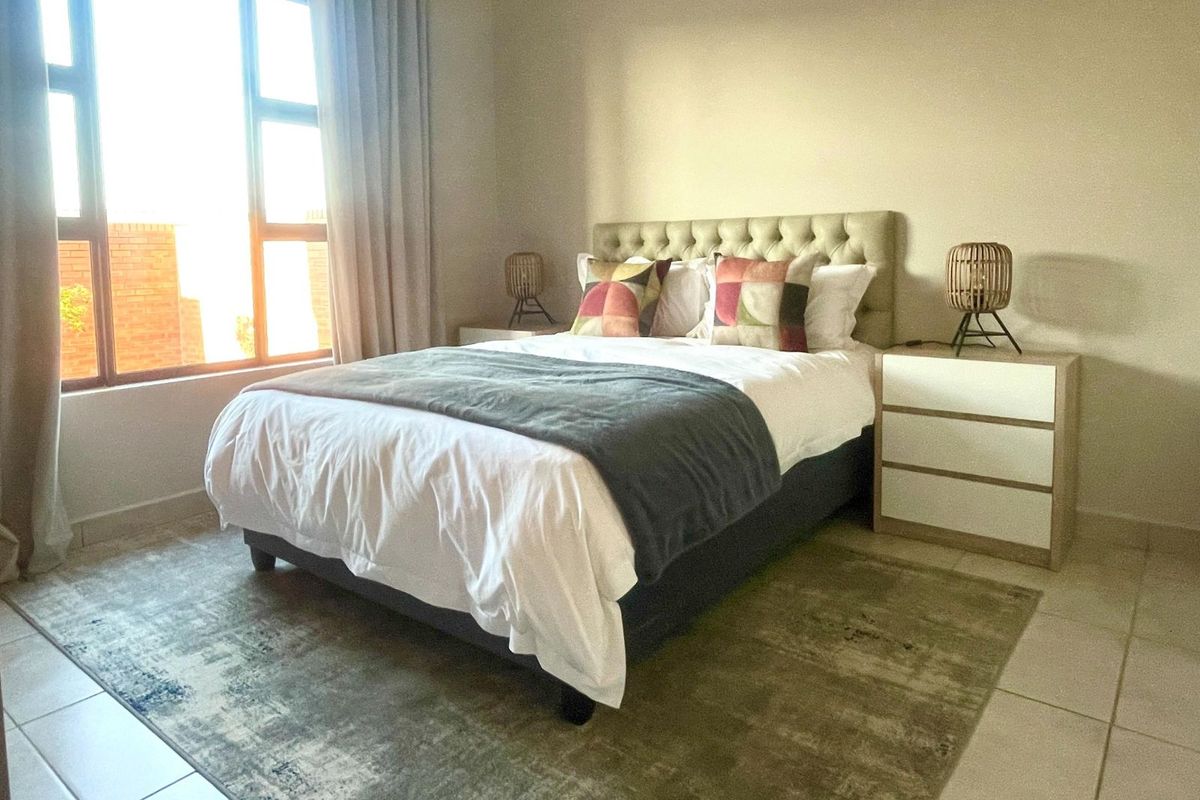 A well-lit bedroom featuring neutral wall tones, tiled flooring, and a large window that allows for ample natural light.
