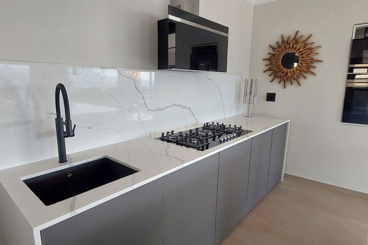 Modern kitchen featuring sleek grey cabinetry, white marble-look stone countertops, a black undermount sink, gas cooktop, and integrated wall-mounted oven and microwave.