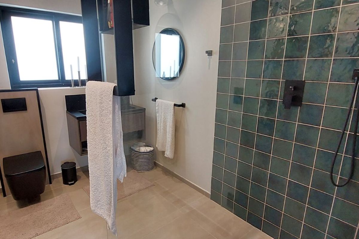 Modern bathroom featuring a walk-in shower with teal decorative tiling, a wall-mounted toilet, and contemporary black fixtures.