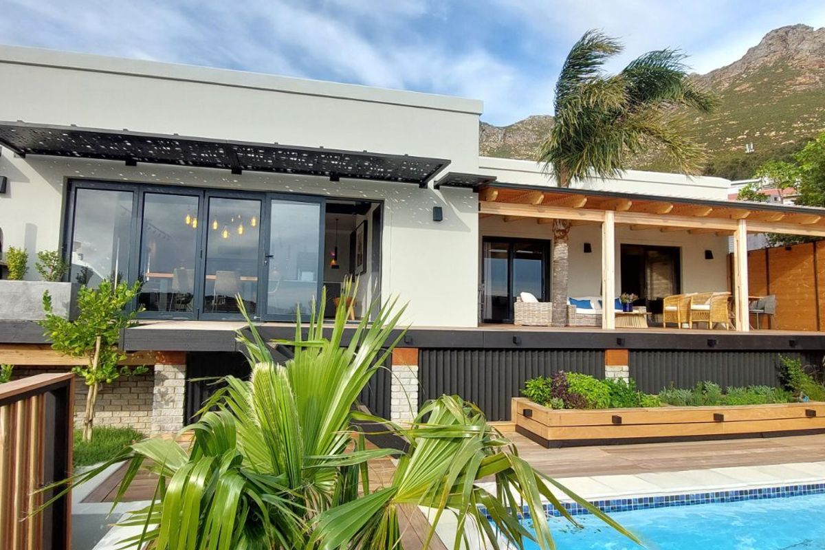 Modern rear exterior featuring a spacious timber deck, covered patio area, swimming pool, and integrated outdoor pizza oven with mountain views.