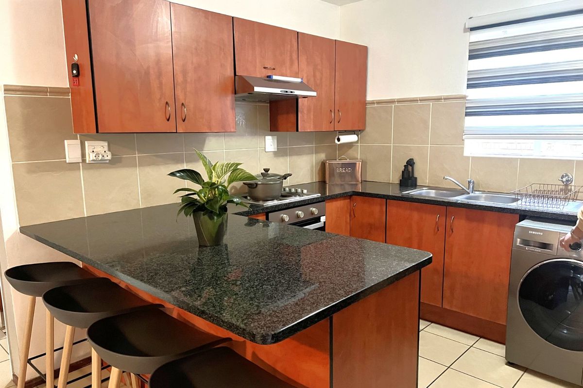 A functional kitchen featuring wooden cabinetry, granite countertops, a breakfast bar, tiled backsplash, and integrated space for laundry appliances.