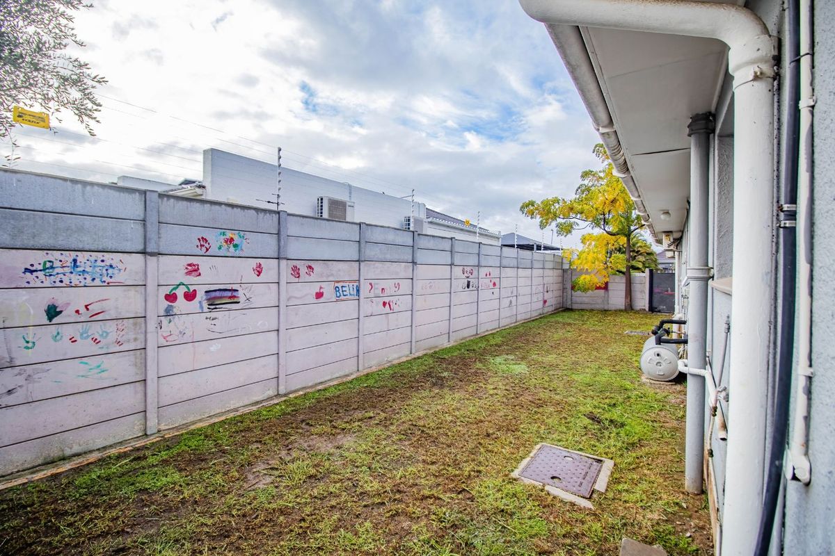 A side garden area featuring a precast concrete boundary wall with visible markings and a small patch of lawn alongside the house exterior.