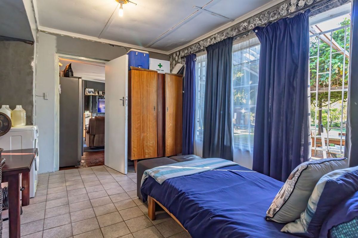 A bedroom featuring tiled flooring, large windows with garden access, and direct entry into an adjacent living space.