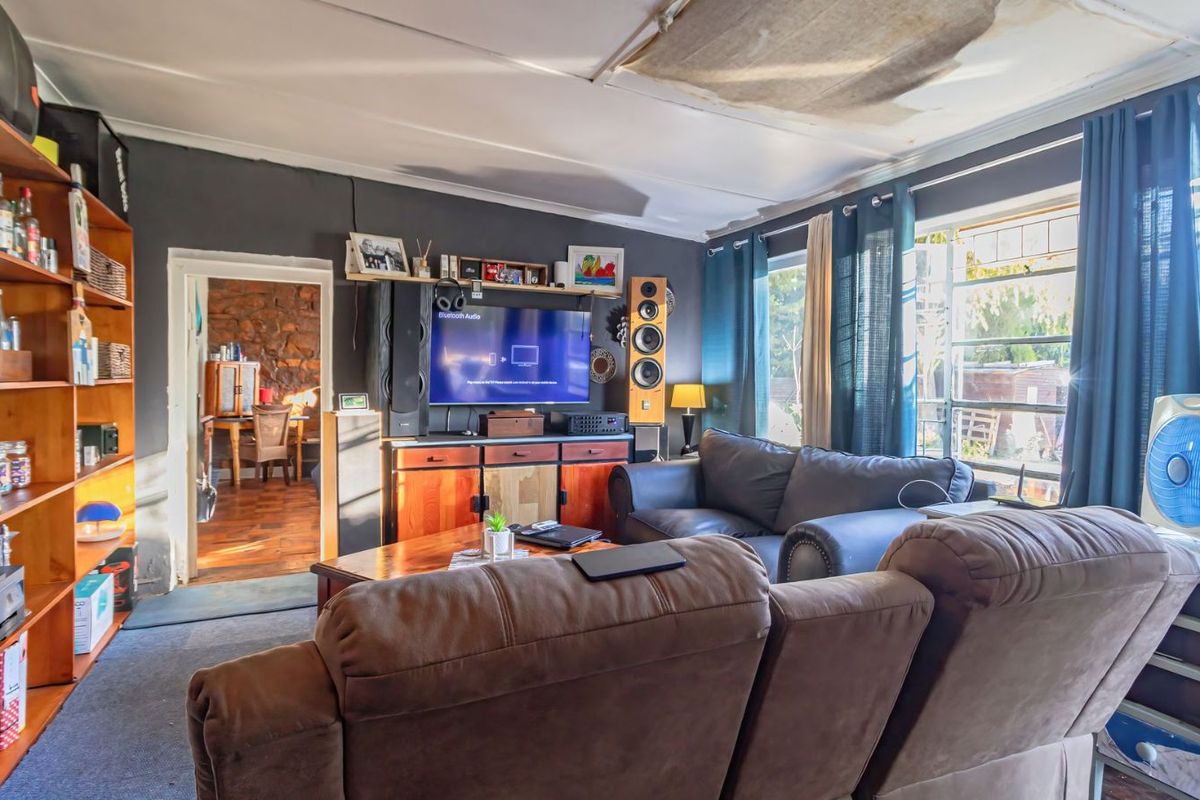 A living room featuring dark walls, large windows with security bars, and a doorway leading to an adjacent room with stone wall accents.