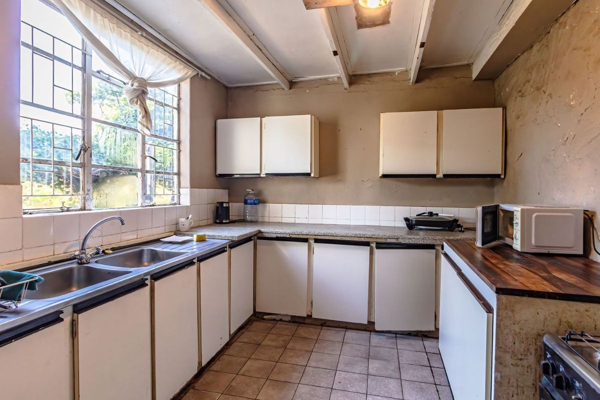 A dated kitchen featuring tiled flooring, laminate countertops, built-in cabinetry, and a double basin sink with a large window providing natural light.