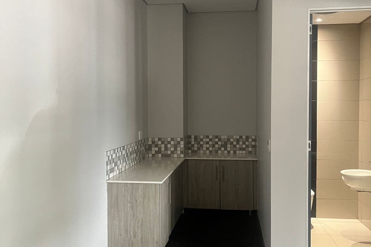A functional office kitchenette area featuring built-in cabinetry, stone countertops, and mosaic tile splashbacks, adjacent to a private restroom facility.