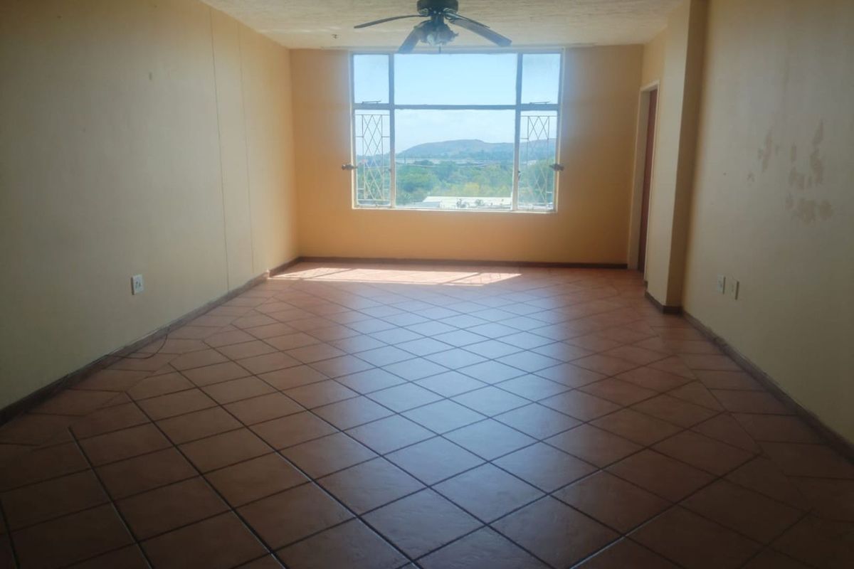 An empty living room featuring terracotta floor tiles, a ceiling fan, and a large window offering scenic views.