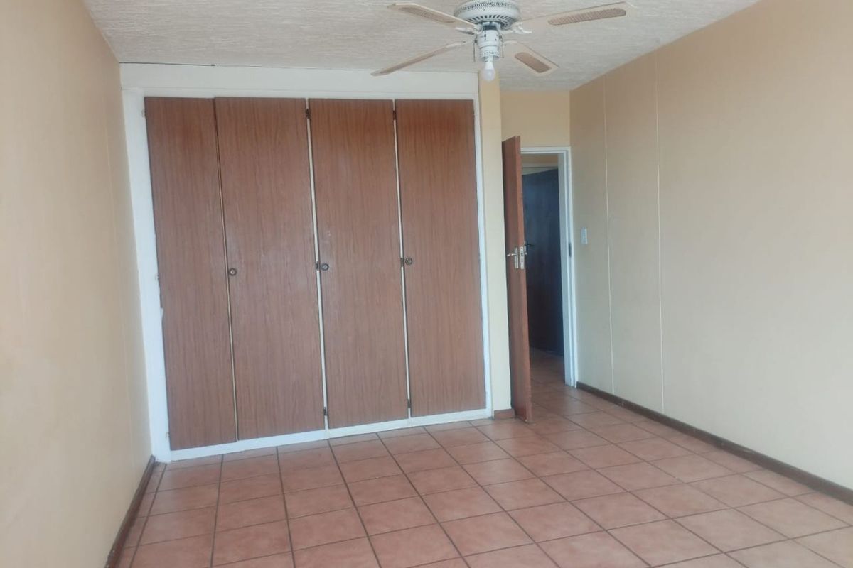 A vacant bedroom featuring built-in wooden wardrobes, tiled flooring, and a ceiling fan, offering a blank canvas for potential updates.