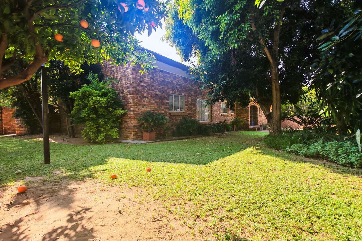 A view of the rear exterior of the house, featuring face-brick walls, established trees, and a spacious garden area.