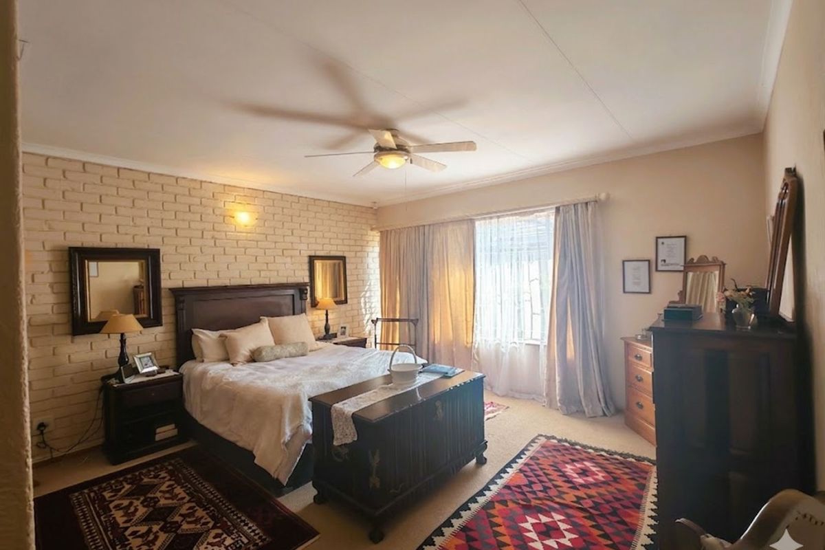 A spacious bedroom featuring a textured brick accent wall, a ceiling fan, and large windows that allow for natural light.