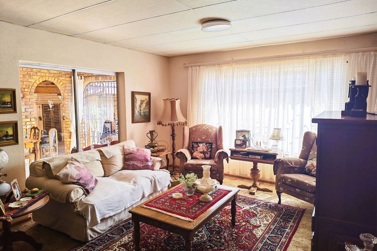 A traditional living room featuring large windows, carpeted flooring, and sliding glass doors that open onto a covered patio area.