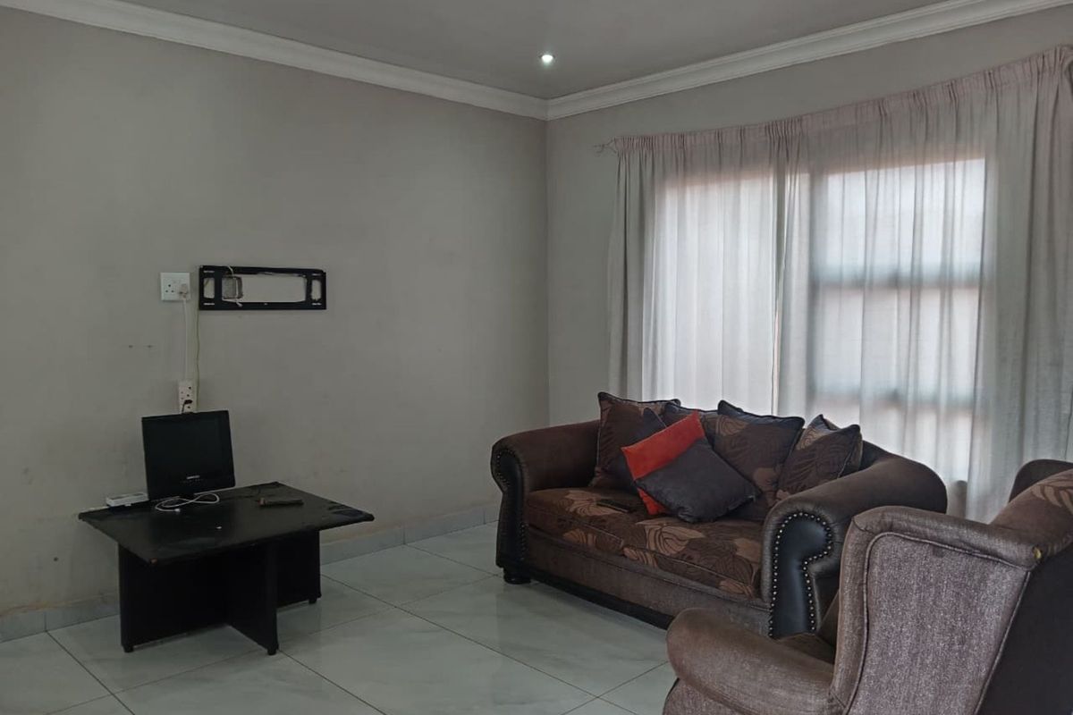 A living room featuring tiled flooring, recessed ceiling lighting, and a large window with curtains, providing a neutral space for relaxation.