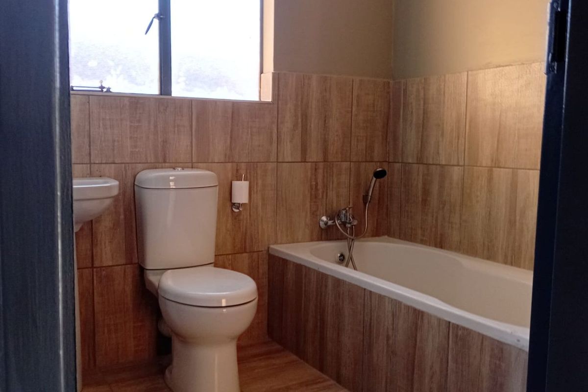 A functional bathroom featuring wood-look wall and floor tiling, a built-in bathtub with handheld shower attachment, and a standard toilet.