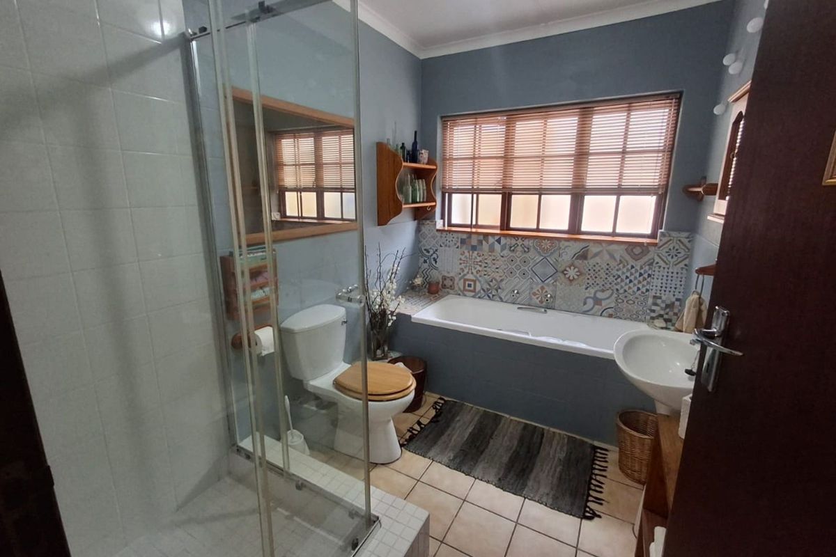 A functional bathroom featuring a glass-enclosed shower, a built-in bathtub with decorative tile backsplash, a pedestal basin, and tiled flooring.
