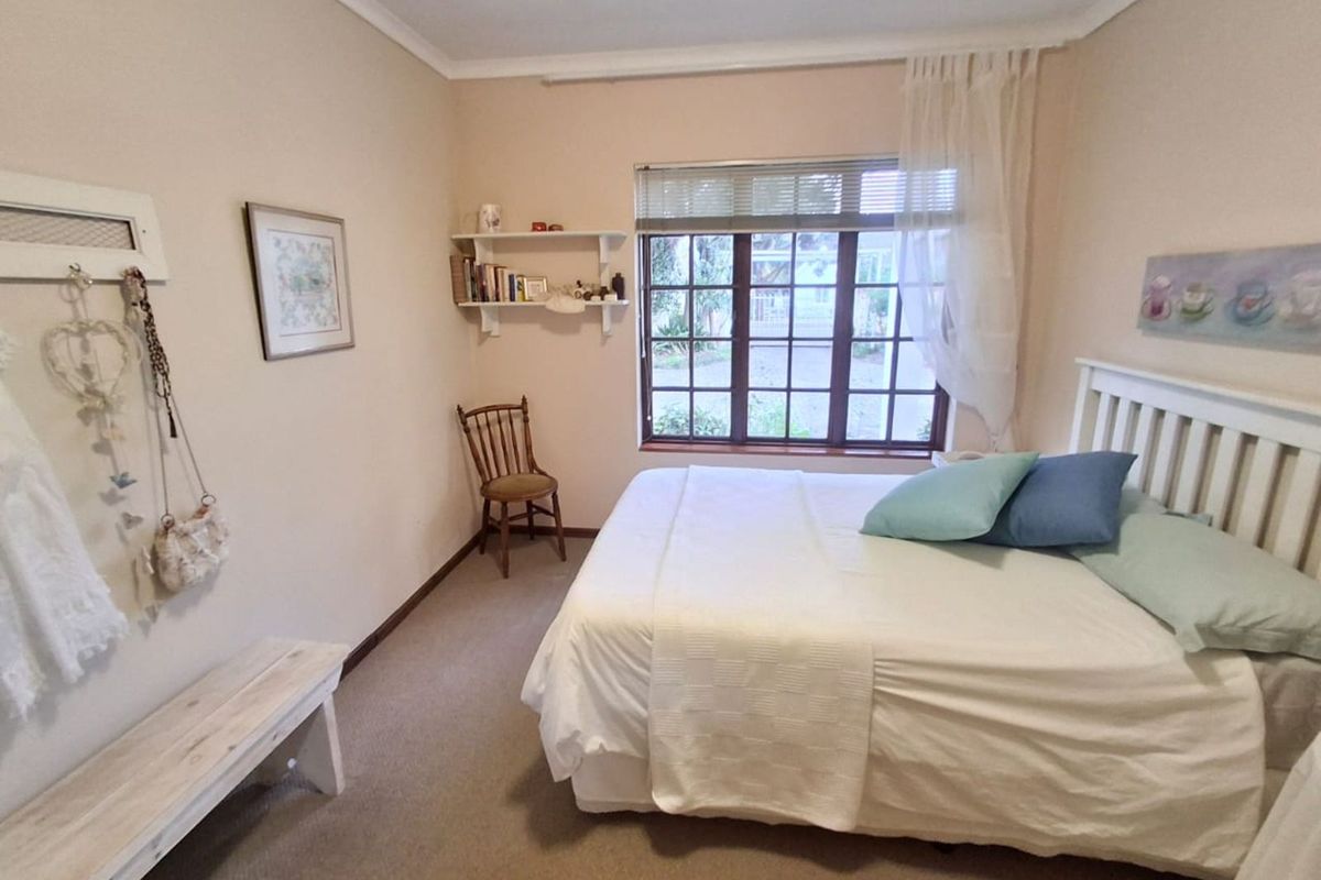 A cozy bedroom featuring neutral walls, carpeted flooring, and a large window with wooden frames providing natural light.